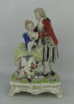 Grupo escultórico em porcelana italiana, policromada e com marca da manufatura de Nápoles, representando "Casal de Idílio". Detalhes em dourado. Base com flores. Med. 18,5x12x10 cm.