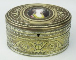 WMF - Porta jóias em metal dourado com delicados trabalhos em relevo e com marca da manufatura na base. Tampa decorada com placa circular em porcelana, com pintura de busto feminino em policromia. Sem fechadura. Med. 7x13x9cm.