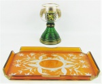 Duas peças em cristal, sendo taça de coleção com brasão e caixa de música suíça, decorada com parreiras e cachos de uva em dourado, e bandeja no tom laranja, lapidada com flores e folhagens em satiné, com arestas vazadas. Alt. taça 16cm e med. bandeja 29,5x18,5cm.
