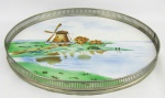Bandeja circular em faiança alemã, com marca da manufatura no verso, decorada com paisagem com moinho de vento em policromia. Gradil em metal prateado. Faltam dois pés, as duas alças e gradil com pequenas mossas. Med. 3,5x32