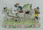 Grupo escultórico em porcelana policromada representando "Carruagem com os três mosqueteiros". Detalhes em dourado. Com discreto fio de cabelo na base e pequenas quebras. Med. 13x23x9cm.