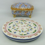 Duas peças, sendo caixa em porcelana oriental policromada e com detalhes em dourado, e descanso de mesa em cerâmica Luis Salvador, decorado com pintura floral em policromia. Med. caixa 10x18x14 e Diam. descanso de mesa 23,5cm.