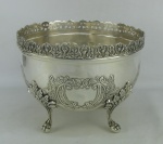Floreira em metal espessurado a prata, decorada com trabalhos em relevo de folhagens e volutas. Borda com vazados. Pés em garra. Med. 21,5x28,5cm.