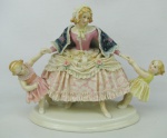 Grupo escultórico em porcelana alemã, policromado, com marca da manufatura Rudolstadt Volkstedt na base, representando "Jovem com crianças". Alt. 20,5cm.