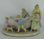 Floreira em biscuit europeu policromado, adornado por figuras representando a brincadeira "cobra-cega". Menino com corpo e uma menina com um braço colado. Quatro dedos da mão do menino, três da mão de uma menina e um dedo de outra menina quebrados. Med. 20,5x31x22cm.
