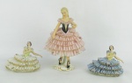 Três estatuetas em porcelana com marca da manufatura Reblis na base, representando "Bailarinas". vestidos trabalhados em rendas. Detalhes em dourado. Com quebras. Alt. maior e menor 18 e 7,5cm.