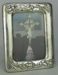 Porta retratos em madeira e prata contrastada, decorada com trabalhos de flores e folhagens em relevo. Prata com pequenas mossas. Med. 18x14cm.