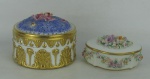 Duas caixas em porcelana portuguesa com trabalhos de flores em relevo e em policromia, com detalhes em dourado, sendo uma circular da manufatura Vista Alegre e outra oval da manufatura Aveiro. Marcadas na base. Pequenas quebras em algumas folhas. Meds. 9x12 e 5,5x11,5x10cm.