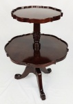 Mesa de apoio em madeira, com 2 platôs, abas recortadas e onduladas. Coluna central entalhada com sulcos e folhagens sobre 3 pernas recurvas terminando em pés na forma de patas. Alt. 80cm. Diam. platôs 61 e 41,5cm.