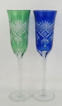 Par de flutes em cristal europeu, sendo um no tom doublet azul e translúcido e o outro verde e translúcido, lapidados com frisos bisotados, olivas, raios e folhagens. Alt. 24cm.