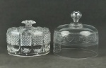 Duas tampas de queijeira, sendo uma em fino cristal Saint Louis, decorado com arabescos, frisos e espirais em satiné e a outra em grosso cristal europeu lapidado em bicos de jaca e dedão, tendo esta pequenos furinhos para ventilação. Med. 15x16 e 11,5x15,5cm.