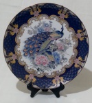 Prato decorativo japonês para parede, em porcelana na tonalidade branca, com desenho de pavão e flores no centro, borda azul cobalto e detalhes dourados. Medida diâmetro 26 cm.