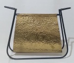 Revisteiro em metal na tonalidade dourada, com detalhes em baixo relevo e suporte em metal preto. Medida altura 38 cm, largura 47 cm e profundidade 12 cm.