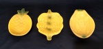 Trio de petisqueiras em porcelana com formato de frutas, sendo, 1 abacaxi, 1 cacho de uva e 1 mamão, todos na tonalidade amarela e detalhes verdes. Medidas aproximadas 18 x 12 cm.