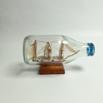 Miniatura artesanal de embarcação na garrafa, garrafa em vidro e navio pintado a mão com base de madeira, vendido no estado conforme fotos. Mede 14 x 6 x 8 cm.