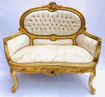 Namoradeira no estilo Luís XV, em madeira entalhada, com pintura dourada e estofado capitonê em tom neutro decorado com arabescos, sinais de uso. Med. 1,05x1,16x0,50 m.