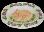 Grande travessa de porcelana com imagem de leitão em relevo e bordas com cachos de uvas. MEDIDA 26x34cm. Apresenta discreto trincado em uma das bordas que não compromete a sua beleza conforme mostra FOTO EXTRA.