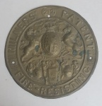 Antigo brasão , adornada com unicórnio, Leão escudo central,  cercado por frases MILNERS 212 PATENT, FIRE RESISTING, data de 1857, feito em latão em alto relevo,  med. 20 centímetros de diâmetro. Placa de cofre antigo com chave da empresa Thomas Milner and Son, fundada em 1830, líder na área da construção de cofres resistentes ao fogo. De formato retangular, possui duas alças nas laterais e uma na parte superior da tampa para ser recolocada com a inscrição Milner & Son Liverpool. Na frente encontramos uma placa de latão gofrada. Este tipo de cofres, frequentemente utilizados em minas, serviam não só para o transporte de valores de todo o tipo (ouro e preciosos), mas também para proteger e transportar documentos importantes, sendo precisamente um cofre à prova de fogo: inicialmente para testar a sua resistência eles o colocam no meio de grandes fogueiras. Durante um incêndio, os materiais contidos nas cavidades da caixa e da tampa (areia, serragem e alume cristal), devido à reação química dos ingredientes, eles garantiram sua resistência até 212 graus Fahrenheit, convertendo 60% do seu volume em vapor. Isso explica o número 212 que vemos na placa: era a referência aos graus que o próprio cofre era capaz de suportar no meio de um incêndio (daí o símbolo, na placa de latão, da Fênix renascendo das cinzas ) em bom estado.