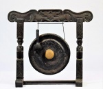 Importante e antigo Gongo de ferro pintado de preto e dourado adaptado a estrutura de madeira na forma de portal, profusamente entalhada adornada por figuras humanas com cara de macaco e dragões. Acompanha martelo de madeira com ponta de fibra natural. Med. 72 x 80 x 28 cm de profundidade. Marcas do uso. Desgastes e pequenas faltas. Nota :A origem do gongo é incerta. A palavra gong é de origem javanesa, mas existem indícios de existência de gongos no sudeste da China desde o século VI. O gongo foi introduzido nas orquestras ocidentais em meados do século XIX, mas nesse contexto ele é frequentemente chamado de tantã (o que cria confusão com o tantã).