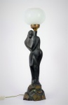 Luminária de mesa composta por escultura de bronze patinado representada por figura feminina, encimada de globo de vidro . Med. 60 x 13 x 14 cm (medidas totais); 12 x 1t5 cm de diâmetro(globo). Parte elétrica não testada. Marcas de uso e do tempo.