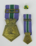 Duas comendas em metal dourado, contendo no verso as inscrições "A Marinha do Brasil A um Marinheiro", e no anverso cena com um barco em relevo. Metal com desgaste causados pelo tempo. Na caixa. Compts. 5,5 e 2cm.