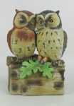 Grupo escultórico em biscuit policromado, representando  "Casal de corujas" . Com caixa de música funcionando. Med. 14x10.5x9.5 cm.