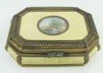 Porta joias europeu, em metal dourado com trabalhos de flores e folhas. Tampa e laterais em baquelite, tendo na tampa pintura miniatura de paisagem sobre celulose. Perdas no dourado. Med. 6x21x15 cm.