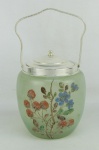 Biscoiteira, anos 60, em vidro fosco verde, decorado com pintura de flores e folhas. Guarnições em metal espessurado a prata. Pequeno amassado na borda da tampa. Med. 24x13,5x13,5 cm