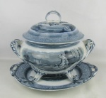 Bela e antiga sopeira com presentoir em porcelana europeia, decoração azul borrão, com pintura de paisagens com castelos, arabescos, volutas e folhagens. Pés recurvos. Med. sopeira 27,5x36x27 cm. Med. presentoir 38x33,5 cm.