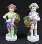 Par de estatuetas em porcelana policromada, representando "Casal de crianças com cestas de flores". Uma apresenta três pequenas perdas nas flores. Alt. 25 e 23,5 cm.