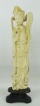 Escultura em marfim oriental, representando "Gueixa com abanico e flores". Apresenta colagem nos arabescos atrás da cabeça. Base em madeira. Alt. total 23,5 cm.