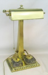 Bela luminária de mesa em bronze e metal banhado de dourado. Apresenta regulagem para a direção da luz, e na base encaixe para dois tinteiros em vidro prensado e na sobre estes, suporte para canetas. Med. 45x27,5x18 cm.