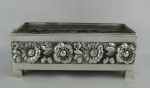 Floreira retangular em metal espessurado a prata, decorada com flores e folhas. Med. 12x31x16 cm.