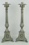 Par de castiçais sacros em metal espessurado a prata, decorados com trabalhos de gomos e sulcos. Bases triangulares, decoradas com bustos de figuras e uma ave.  Pés na forma de cabeça de animais. Pequenos desgastes no prateado e bobeche de um com mossas.  Alt. 39,5 cm.