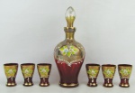 Conjunto de licoreiro e 6 copinhos em vidro veneziano, no tom vermelho, decorados com pintura floral policromada em relevo e ricos detalhes em dourado. Pequenos desgastes no dourado. Alt. licoreiro 24 cm.