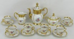 Serviço para café em porcelana Real, com decoração floral em policromia e ricos detalhes em dourado, composto de bule, leiteira, açucareiro e 6 xícaras para café. Alt. bule 17,5 cm.