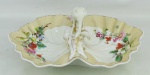 Petisqueira em porcelana europeia, com marca da manufatura na base, decorada com pintura floral em policromia, e ao centro uma ave, flores e folhagens em alto relevo. Borda com ondulações. Detalhes em dourado. Ponta do bico da ave quebrado. Med. 12x33x25,5cm.