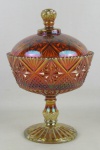Compoteira em vidro prensado rouge de fer, com lapidações de gomos, sulcos e bico de jaca. Tampa com lascado na parte interna da borda e base com trincado. Alt. 21,5cm.
