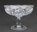 Fruteira de pé alto em cristal translúcido, lapidada com rosetas, sulcos e estrelas. Haste sextavada. Med. 15,5x19,5cm.