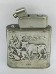 Antigo isqueiro de mesa, em prata européia, contrastada, cinzelada com cenas de boiadeiros em relevo. Guarnições em metal. Mecanismo necessita reparo. Med. 9,5x8x3cm.