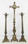 Antigo terno sacro em bronze composto de crucifixo com cristo vivo e par de tocheiros, com trabalhos em gomos, folhas e volutas. Bases triangulares, tendo em cada face figura sacra em relevo. Alt. crucifixo 72,5cm. Alt. tocheiro 54cm.