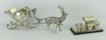 Duas peças decorativas em metal espessurado a prata, sendo trenó com cervo e carroça com cavalos. Cervo com uma pata quebrada e carroça com desgastes no prateado. Meds. 11x23x5 e 5,5x11,5x5cm.