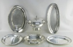 a) Sopeira em metal espessurado a prata com marca da manufatura Wolff, decorada com trabalhos de sulcos, laços de fita, X, volutas e folhas em relevo. Med. 22x32,5x25,5cm. b) Cinco peças de baixela em metal espessurado a prata, com marca da manufatura Fracalanza, sendo legumeira, prato para arroz e 3 travessas ovais, decorados com gomos e X em relevo. Med. travessa maior 46,5x30,5cm.