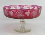 Fruteira de pé alto em cristal no tom lilás, decorada com lapidações de folhas de parreiras e cachos de uva em satiné. Haste e base translúcidas. Minúsculo bicadinho na borda. Med. 14,5x23cm.