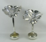 Dois solifleurs em metal espessurado a prata, com marca da manufatura na base. Parte superior com trabalhos representando uma flor. Desgastes no prateado. Alts. 40 e 34cm.