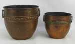 Dois cachepots em cobre martelado, decorados com trabalhos de flores em relevo. O menor com pequena mossa na base. Meds. 18,5x22cm e 14,5x15,5cm.