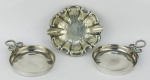 a) Cinzeiro em prata  com resquícios do contraste e do teor, decorado com trabalhos de flores, folhas e gomos curvos. Med. 9x8,5cm. peso 25g. b) Christofle - Par de petisqueiras em metal francês, com marca da manufatura no verso. Alças trabalhadas com retorcidos. Med. 2x10x7cm.