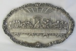 Placa ovalada em metal espessurado a prata, tendo ao centro em relevo a Santa Ceia. Borda com trabalhos de flores e folhas. Med. 29x45 cm.