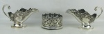 Três peças, sendo par de molheiras em metal inglês, espessurado a prata, com marca da manufatura Sheffield plate, decoradas com flores, folhagens e volutas em relevo, e porta garrafa em metal numerado, com fundo em madeira, trabalhado com volutas, perolados e vazados. Pequenos desgastes no prateado e porta garrafa com mossas na base. Alts. 15 e 8cm.
