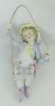 Estatueta em porcelana européia, policromada, representando "menino no balanço". Minúsculo bicado na borda de trás do chapéu e pequenas perdas nas flores. Alt. 24,5cm.